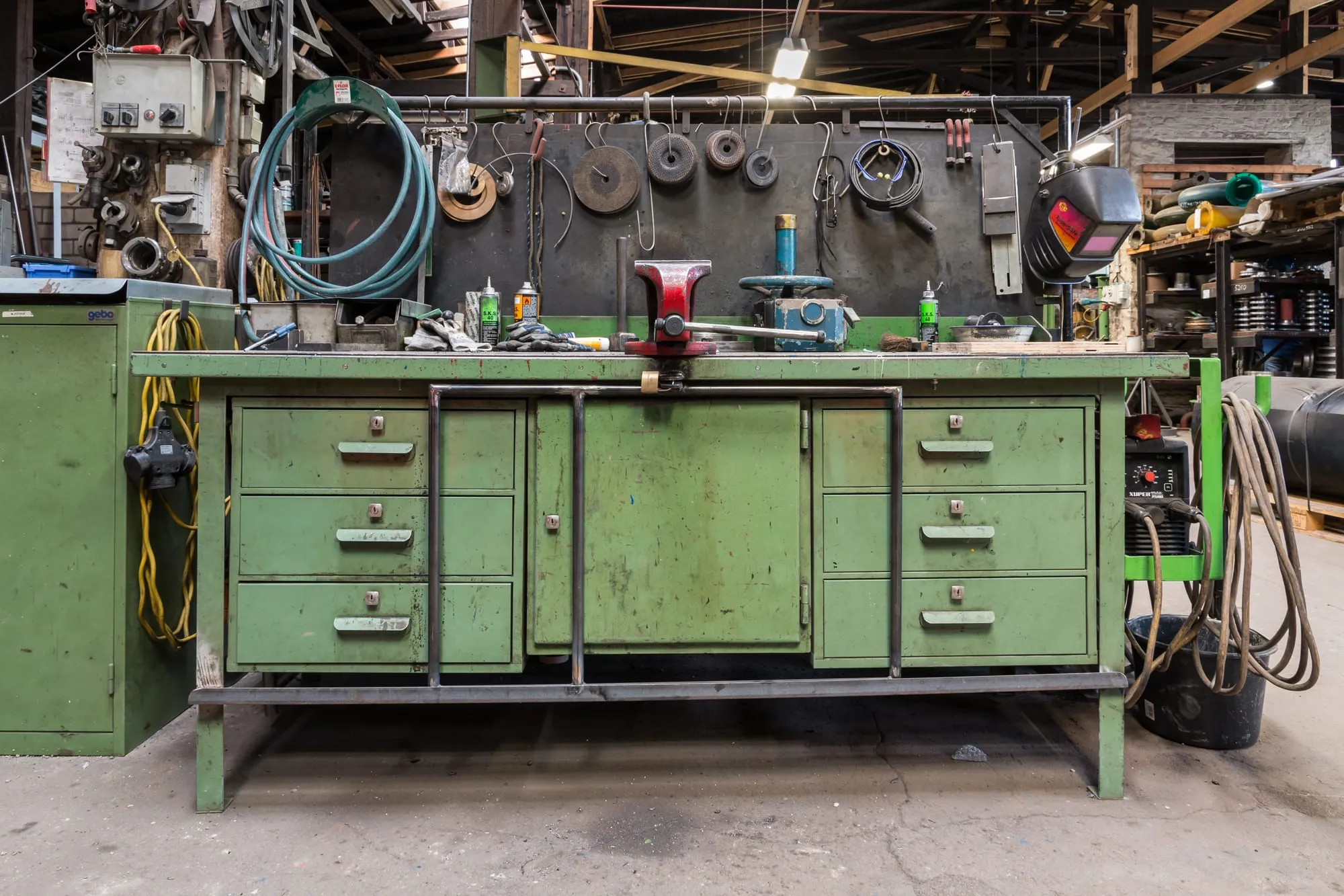 Un établi vert et un mur d’outils dans un atelier industriel